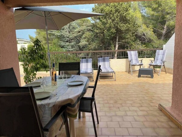 Un patio al aire libre con una mesa de comedor para dos personas, rodeado de sillones reclinables a rayas.
