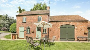 A brick building with a green door, a large umbrella, and a table with chairs in the front yard. - Escape to this exquisite holiday let in Tetford. (Tetford, near Horncastle)
