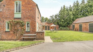 A brick building with a green window, a bench, and a lawn area with a table and chairs. - Escape to this exquisite holiday let in Tetford. (Tetford, near Horncastle)