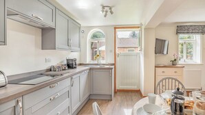 A modern kitchen with grey cabinets, a built-in oven, and a dining area with a table set for breakfast. - Escape to this exquisite holiday let in Tetford. (Tetford, near Horncastle)