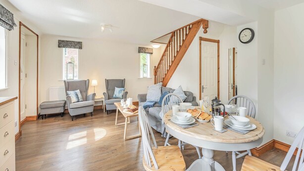 A spacious living area with a wooden staircase, a dining table set for breakfast, and a cozy seating arrangement. - Escape to this exquisite holiday let in Tetford. (Tetford, near Horncastle)