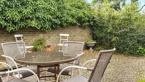 A patio with a round table and wicker chairs, surrounded by a brick wall and greenery. - 2 bedroom accommodation in Beadnell, near Alnwick (Beadnell, near Alnwick)