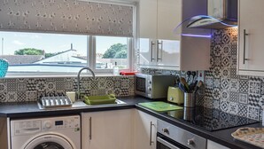 A compact kitchen with a washing machine, a toaster, and a sink. - 2 bedroom accommodation in Beadnell, near Alnwick (Beadnell, near Alnwick)