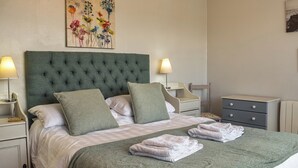 A neatly made bed with a green headboard, two bedside tables with lamps, a small wooden chair, and a nightstand with a lamp. - 2 bedroom accommodation in Beadnell, near Alnwick (Beadnell, near Alnwick)