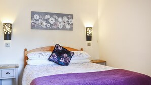 Un letto rifatto con una coperta viola, un cuscino floreale e un quadro appeso al muro sopra di esso.