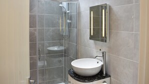 Un bagno moderno con cabina doccia in vetro, un lavandino bianco e uno specchio a parete.