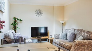 Un soggiorno moderno con una TV a schermo piatto, un tavolino in legno, un divano e una poltrona a fantasia.
