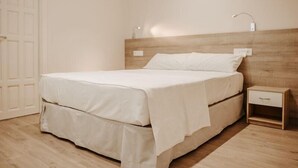 Een net opgemaakt bed in een kamer met een houten hoofdbord, een nachtkastje met lade en een deur op de achtergrond.
