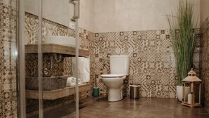 Een badkamer met patroon tegels, een toilet, een glazen douchecabine en een potplant.
