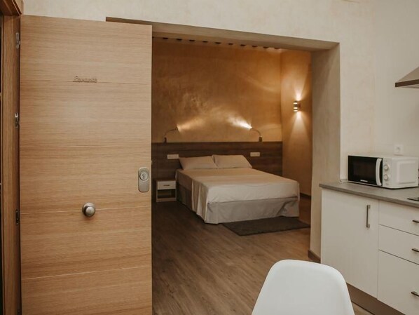 A compact room with a bed, a microwave, and a small kitchenette.