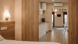 A hotel room with a wooden headboard, a bedside lamp, a bed, a kitchenette with cabinets, a flat-screen TV, and a view of the balcony. - Apartamento 1 dormitorio y 2 sofas cama Atlántica (Valdepeñas)
