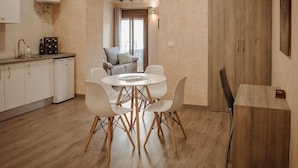 A modern kitchen with white cabinets, a dining table with white chairs, and a wooden floor. - Apartamento 1 dormitorio y 2 sofas cama Atlántica (Valdepeñas)