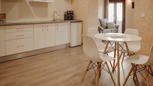 A modern kitchen with white cabinets and a wooden floor. There is a dining area with a round table and four chairs. - Apartamento 1 dormitorio y 2 sofas cama Atlántica (Valdepeñas)