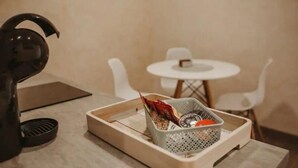 A room with a small table, chairs, a kettle, and a tray with a basket containing various items. - Apartamento Deluxe Mediterránea (Valdepeñas)