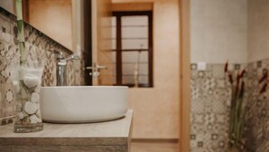 A bathroom with a large white sink, a glass vase with white stones, and a potted plant with tall green leaves. - Apartamento Deluxe Mediterránea (Valdepeñas)
