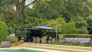 Piscina com área de terraço coberta, móveis de vime e churrasqueira.