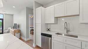 A modern kitchen with white cabinetry, a stainless steel dishwasher, and a large island with a marble countertop.