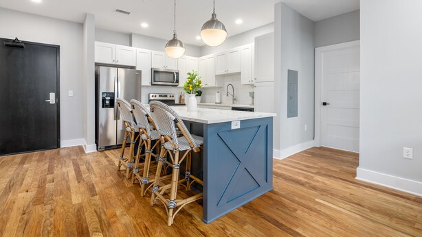 A modern kitchen with white cabinets, a central island with bar stools, stainless steel appliances, and pendant lighting.
