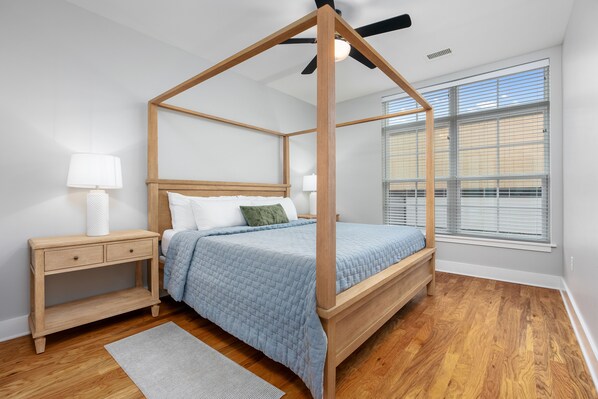 Une chambre à coucher avec un lit à baldaquin, une table de chevet, une lampe de chevet et une fenêtre avec des stores.