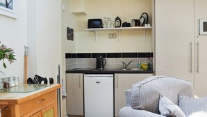 A compact kitchen with a refrigerator, microwave, and sink. There is a small dining area with a chair and a table. - Gracies Cottage - UK44686 (Beamish)