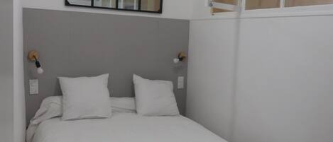 Un dormitorio con cama, espejo y ventana.
