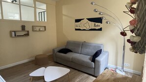 A living room with a grey sofa, two white chairs, a wooden coffee table, a wall-mounted lamp, and a decorative wall piece. - T2 Rénové Hyper Centre, à 50 m de la Cathédrale (Rodez)