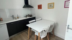 A compact kitchen with a white countertop, black cabinets, and a black range hood. There is a white dining table with two chairs. - T2 Rénové Hyper Centre, à 50 m de la Cathédrale (Rodez)
