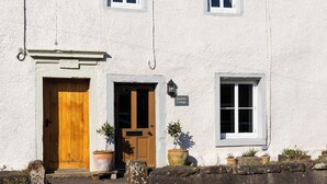 Ein weißes Gebäude mit einer Holztür, einem kleinen Fenster und einem Schild mit der Aufschrift 'Earsdon Cottage'.