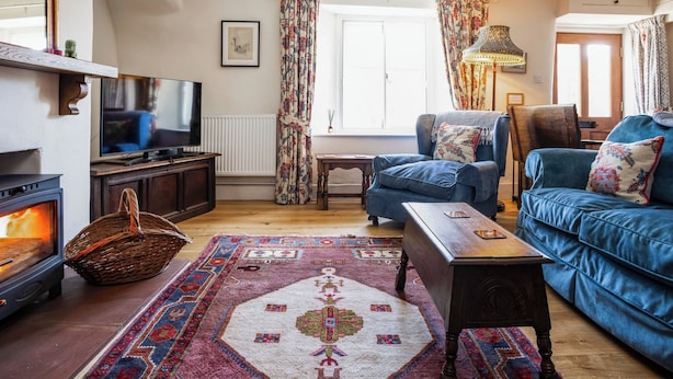 Ein gemütliches Wohnzimmer mit Kamin, blauen Sofas, einem Fernseher und einem gemusterten Teppich.