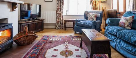 A cozy living room with a fireplace, blue sofas, a television, and a patterned rug.