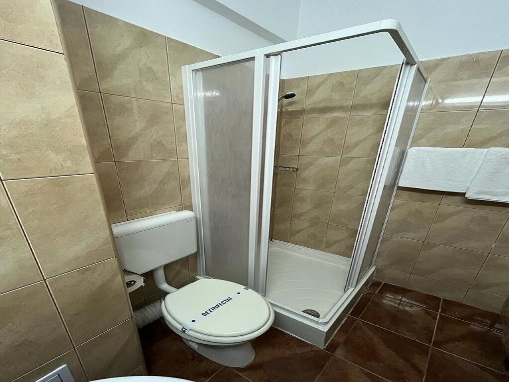 A bathroom with a white toilet, a glass-enclosed shower, and beige tiled walls.