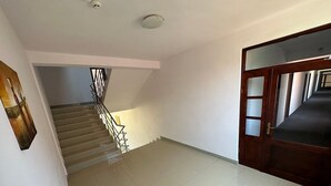 A spacious hallway with a staircase leading to another floor, a wooden door with glass panels, and a ceiling light fixture. - Hostel Stefania (Costinesti)
