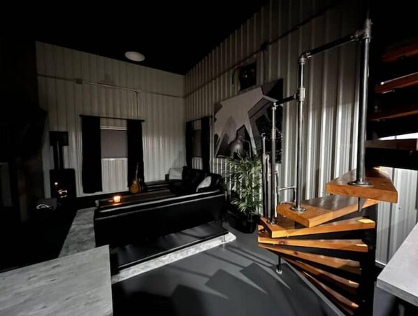 Una sala de estar moderna con un sofá negro, una mesa de centro y una escalera con escalones de madera.