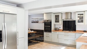 Una cocina moderna con armarios blancos, horno empotrado y un comedor con banco.