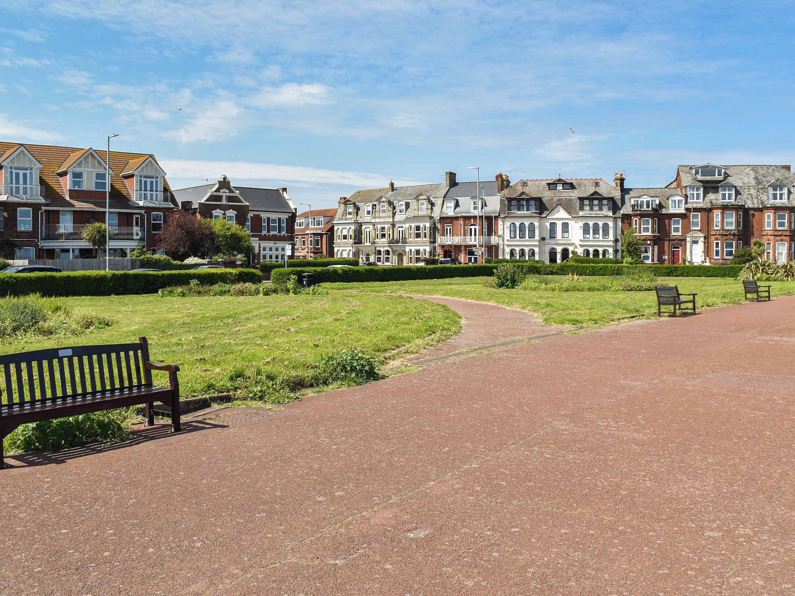 A park with a paved path, benches, and a row of historic houses.