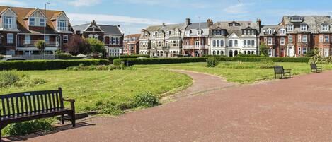 A park with a paved path, benches, and a row of historic houses.