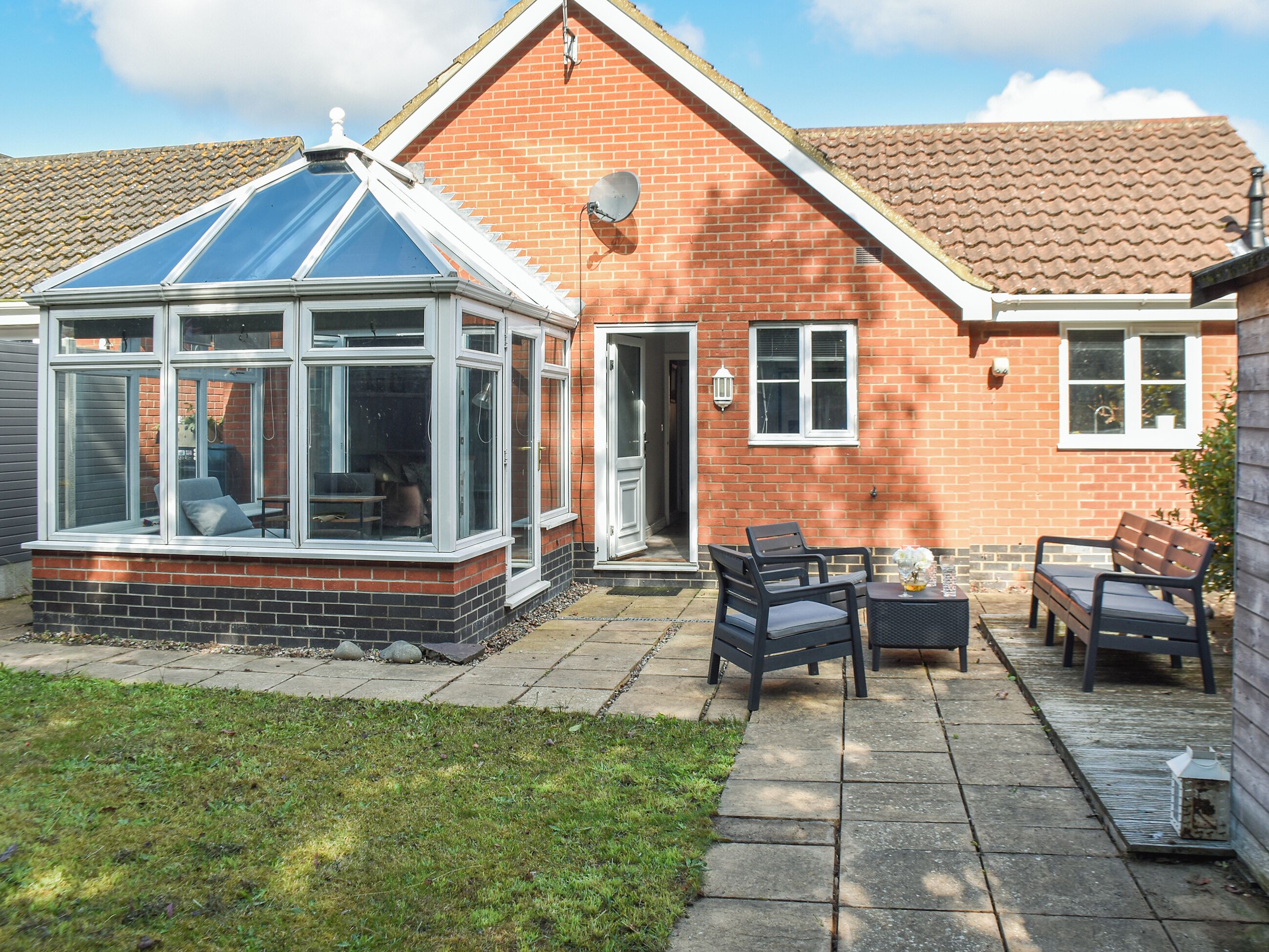A conservatory with a glass roof, a brick house with a tiled roof, and outdoor seating with a table and chairs.