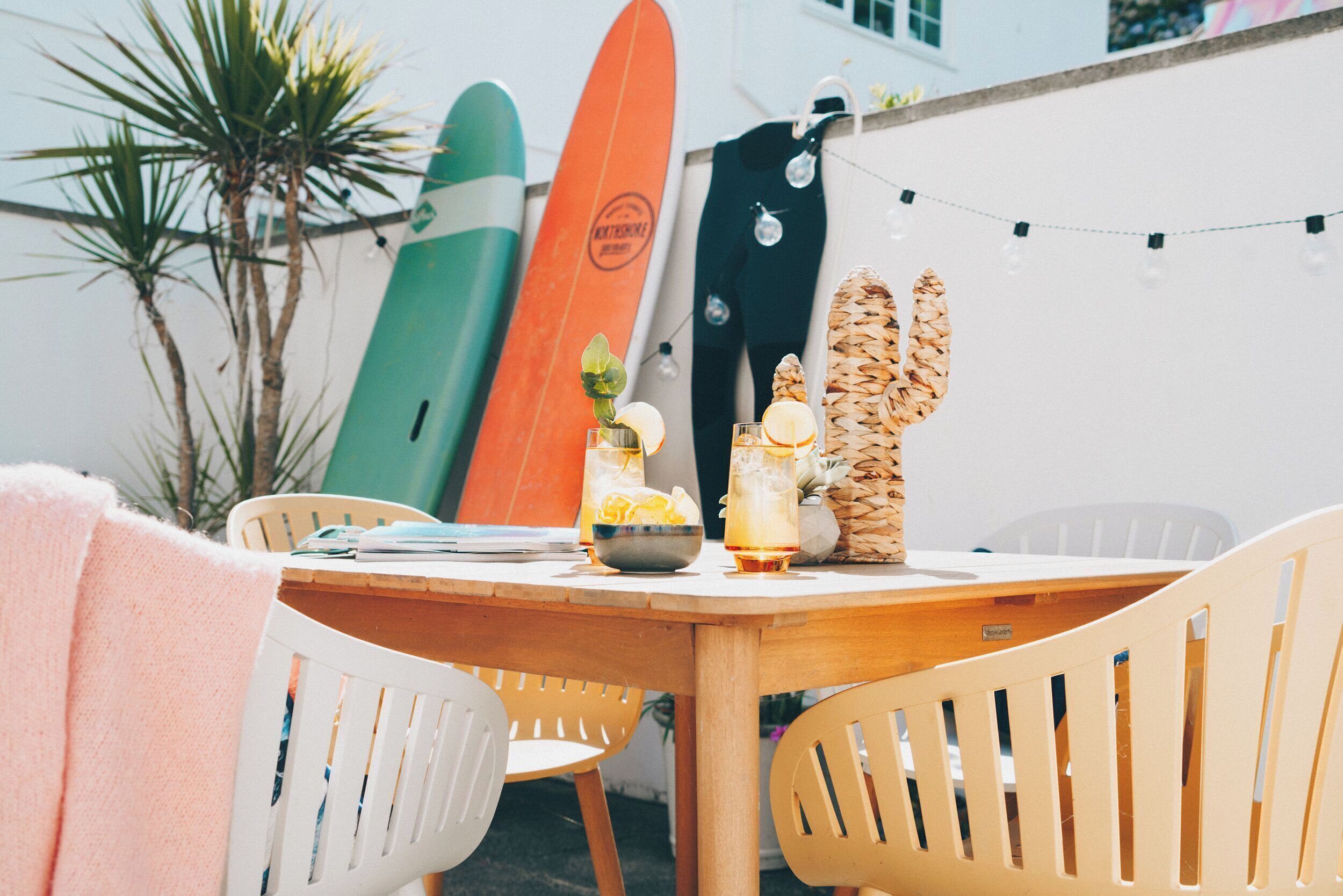 A wooden table with chairs, a surfboard, and a tiki statue.
