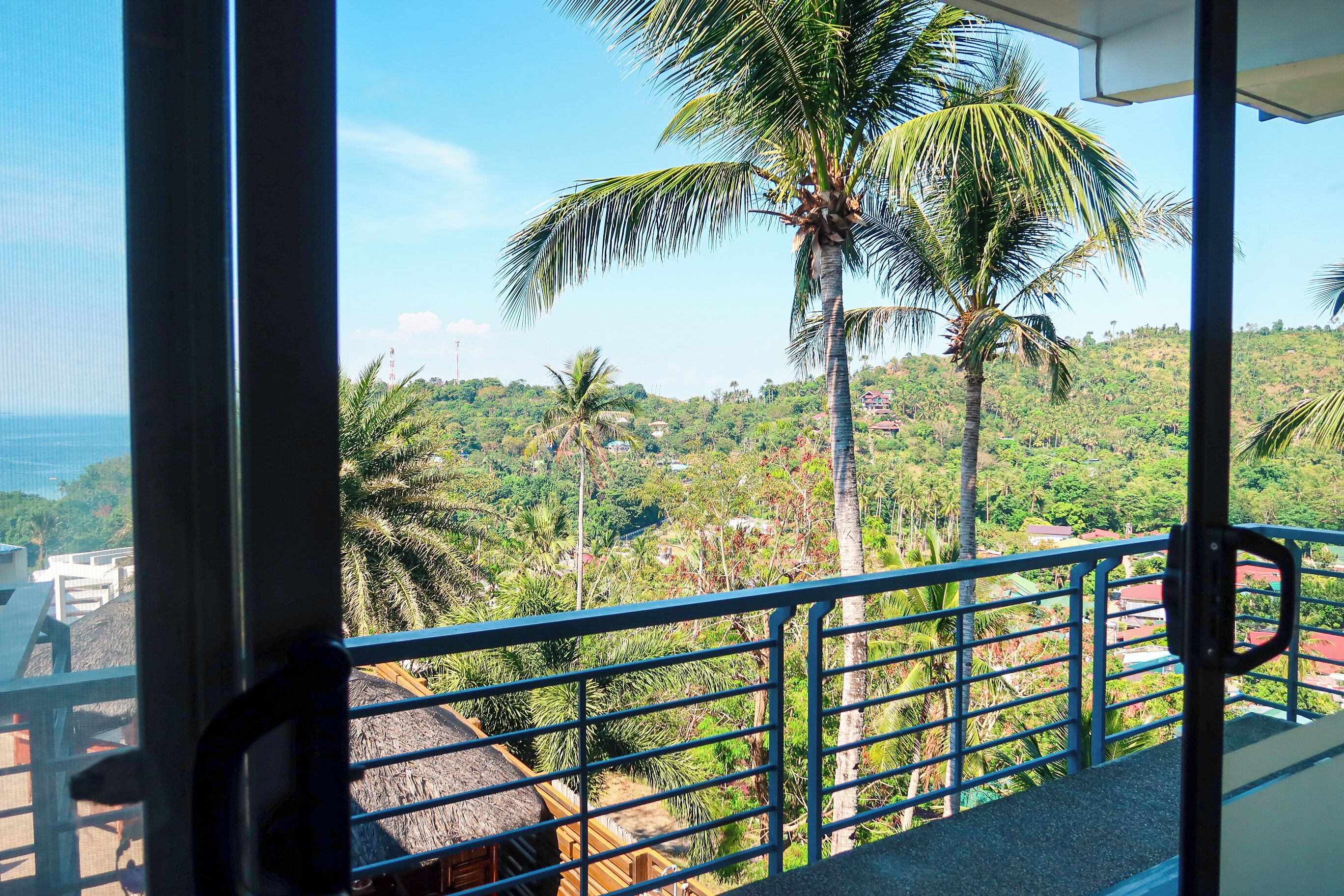 Un balcón con vista a un paisaje verde exuberante, con palmeras y una vista distante del océano.
