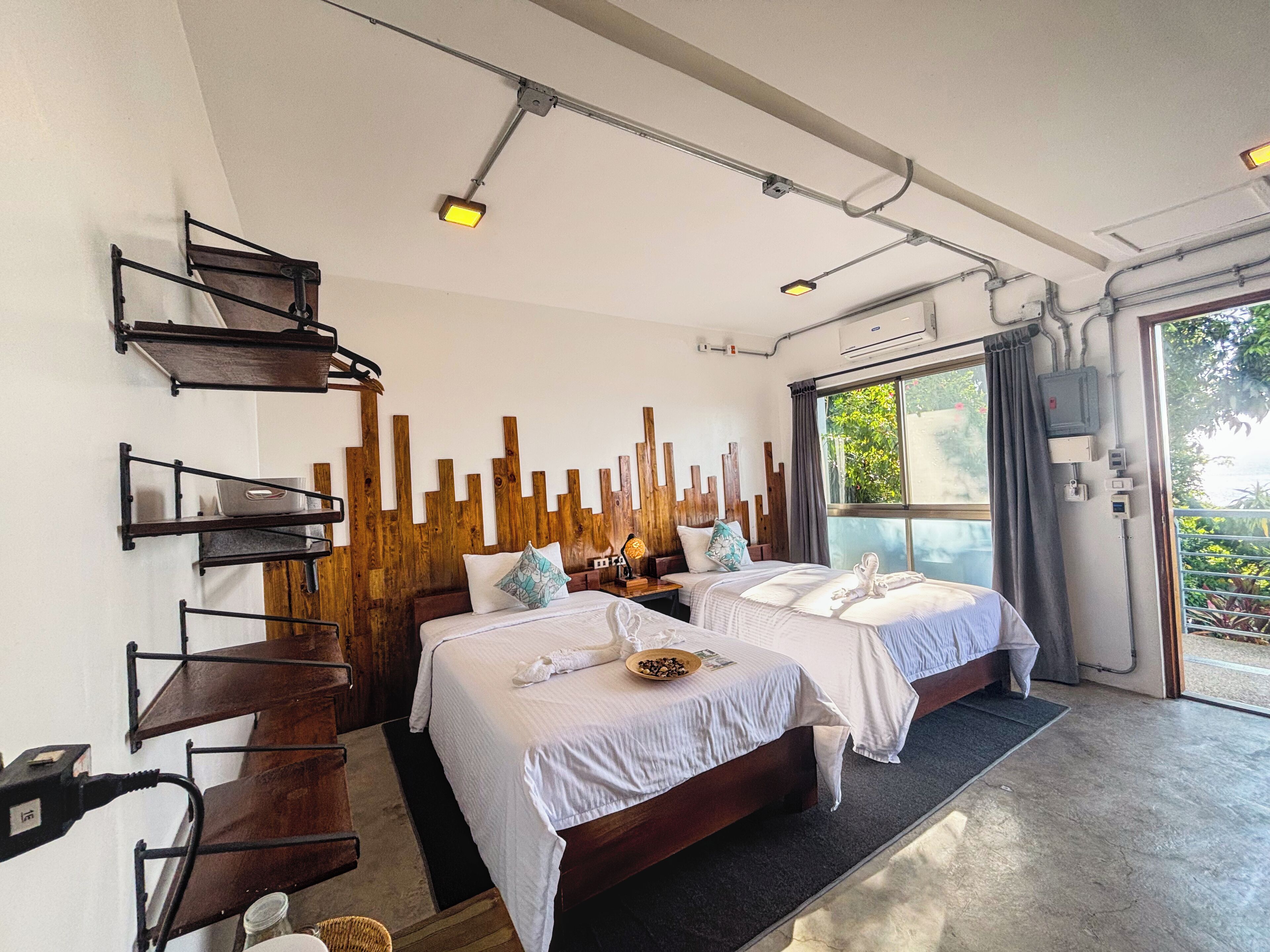 A modern hotel room with two beds, a wooden accent wall, and a large window offering a view of greenery.