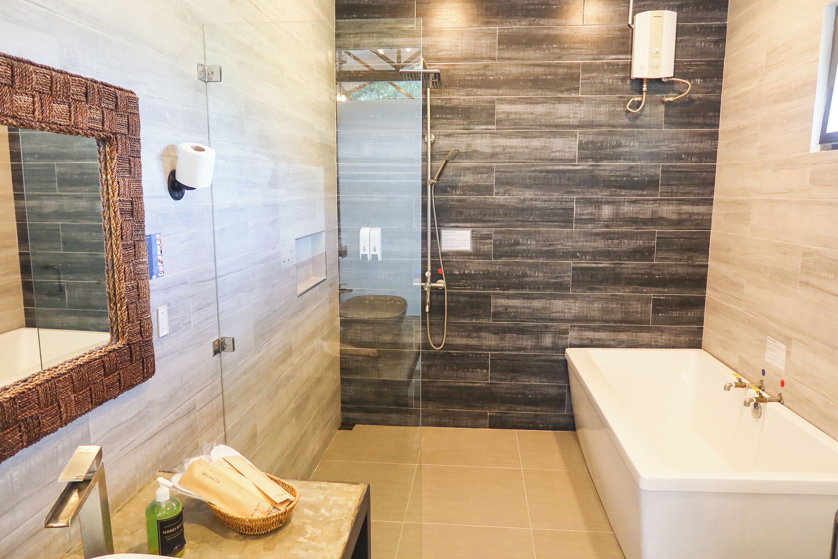 A modern bathroom with a large mirror, a bathtub, a shower area, and a vanity with toiletries.