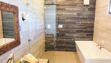 A modern bathroom with a large mirror, a bathtub, a shower area, and a vanity with toiletries.