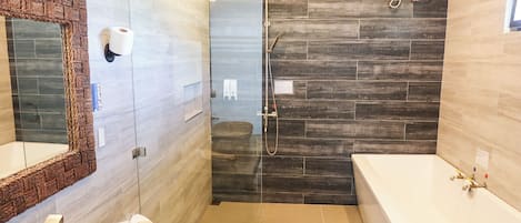 A modern bathroom with a large mirror, a bathtub, a shower area, and a vanity with toiletries.