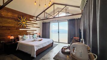 A spacious bedroom with a large bed, wooden wall decor, a ceiling light fixture, and a view through the glass door.