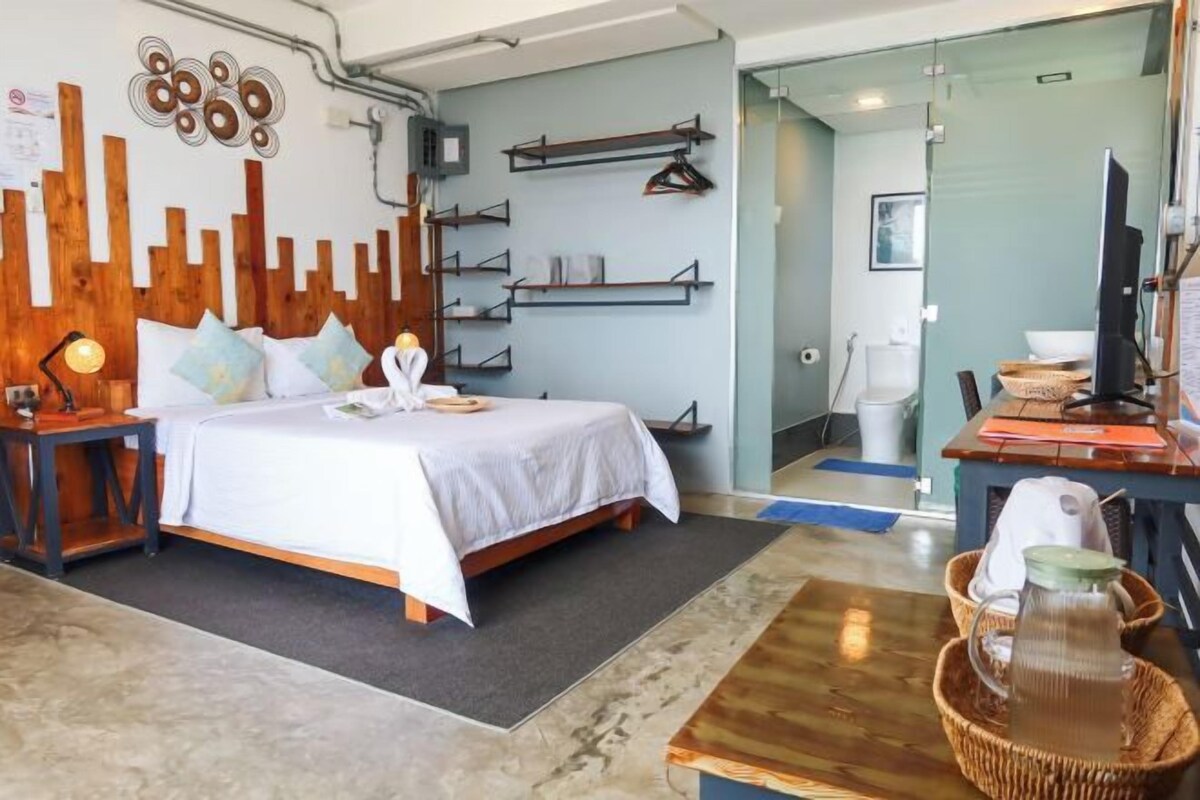 Una habitación de hotel moderna con cama, mesitas de noche, escritorio y baño visible a través de una puerta abierta.