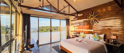 A spacious bedroom with a large bed, a wooden headboard, and a view of the outdoors through floor-to-ceiling windows.