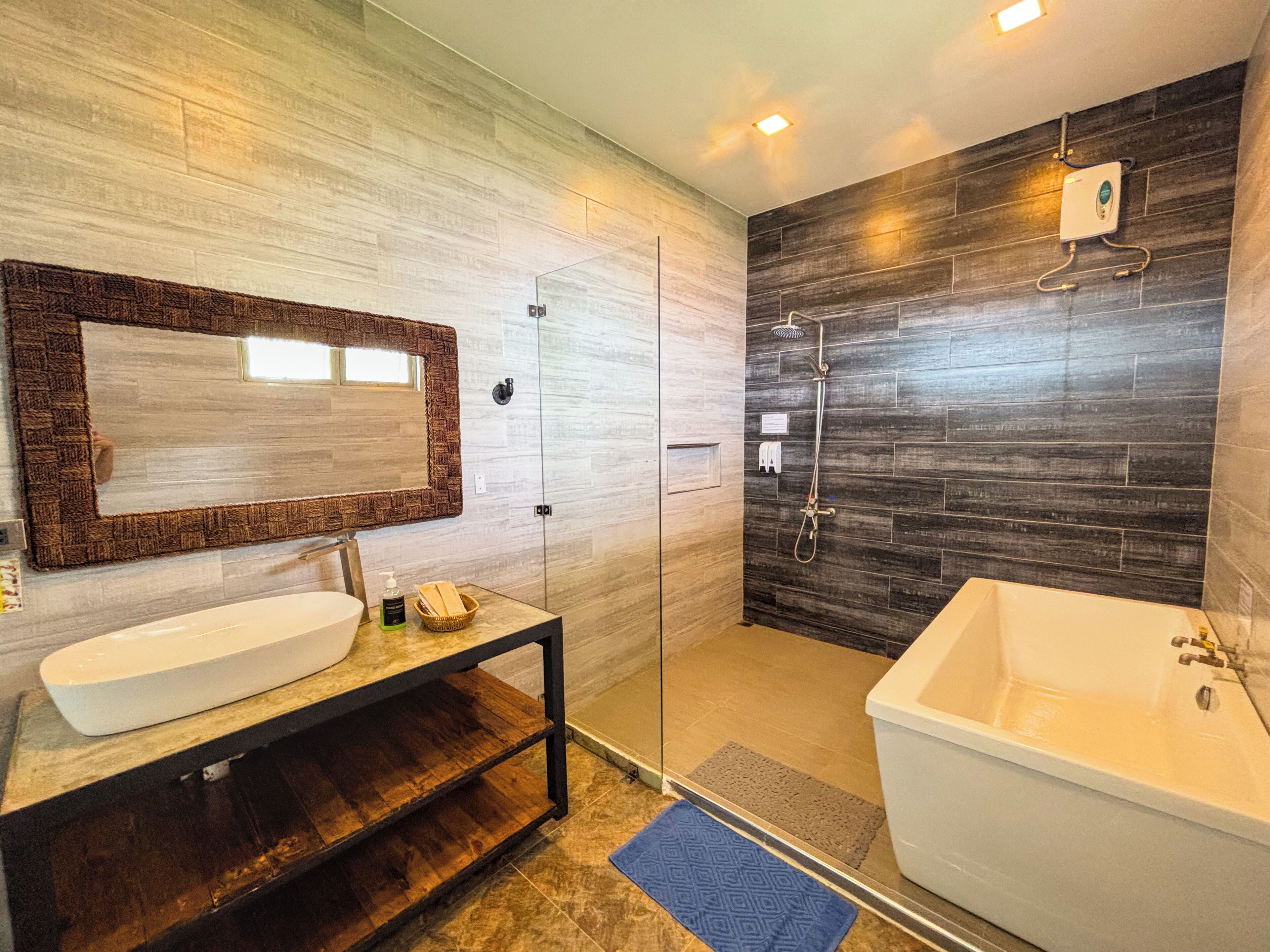 A modern bathroom with a large mirror, a white sink, a wooden vanity, a glass-enclosed shower, and a bathtub.