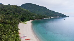 A beach with boats lined up, a sandy shore, and a forested hill in the background. - AV Suites (Puerto Galera)