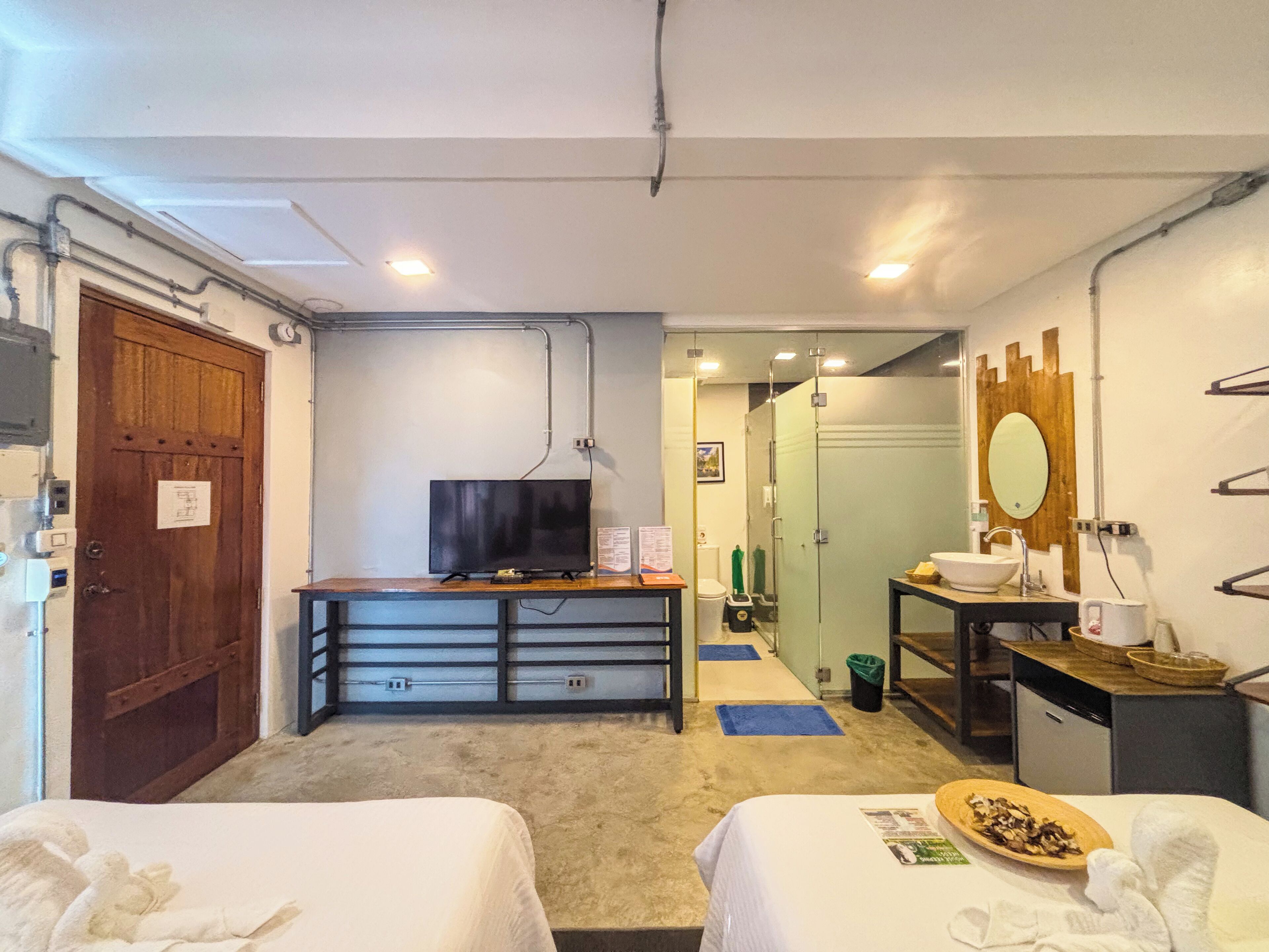 A hotel room with two beds, a television, a small table, a sink, and a mirror.