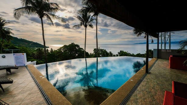 An infinity pool with a view of the ocean and palm trees. - AV Suites (Puerto Galera)